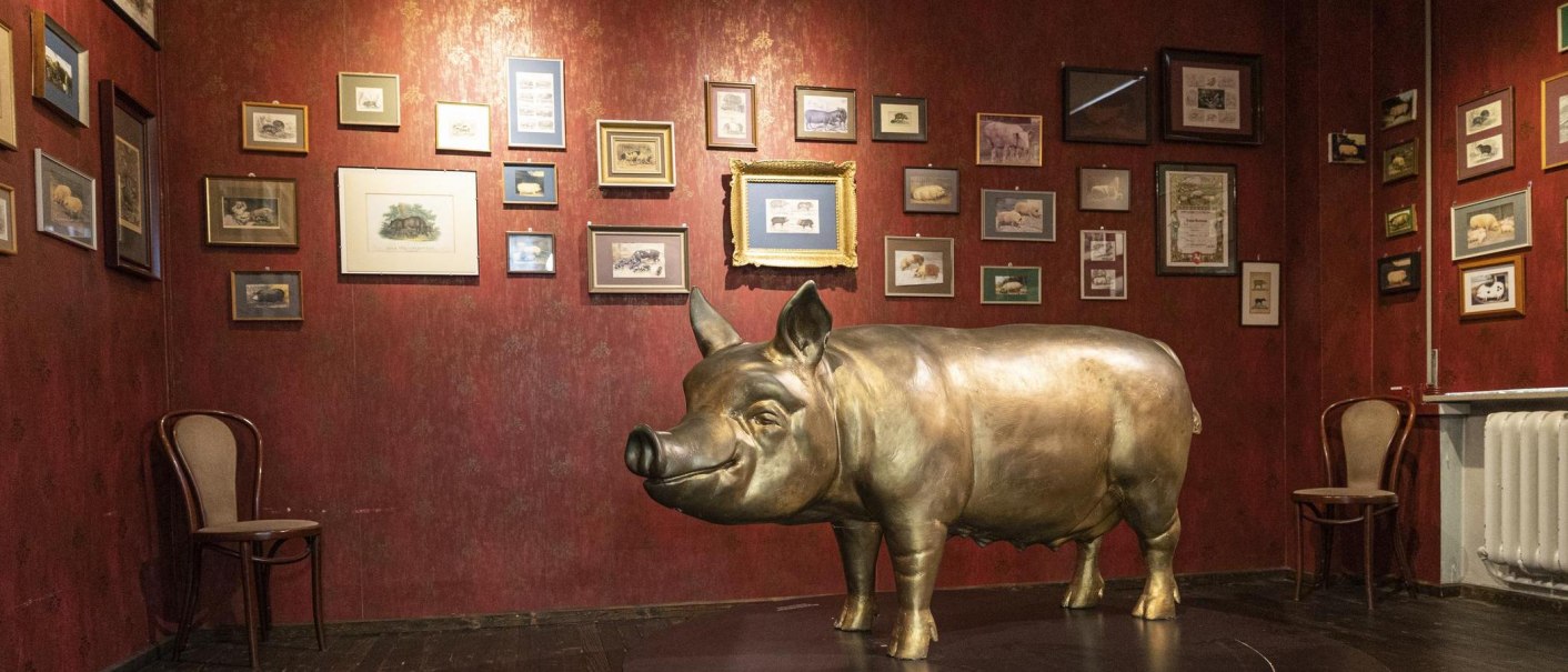 A room in the Stuttgart Pig Museum with a large pig sculpture and numerous framed pictures on a red wall., &copy; Stuttgart-Marketing GmbH, Sarah Schmid