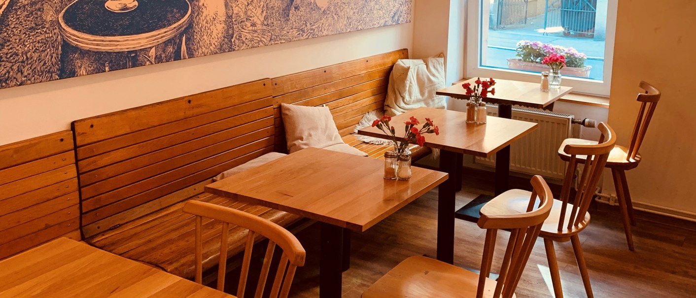 Gem&uuml;tlicher Innenbereich eines Caf&eacute;s mit Holztischen und -st&uuml;hlen, Blumenvasen auf den Tischen und einem gro&szlig;en Fenster mit Blick nach drau&szlig;en., &copy; Gustav Gastro GmbH