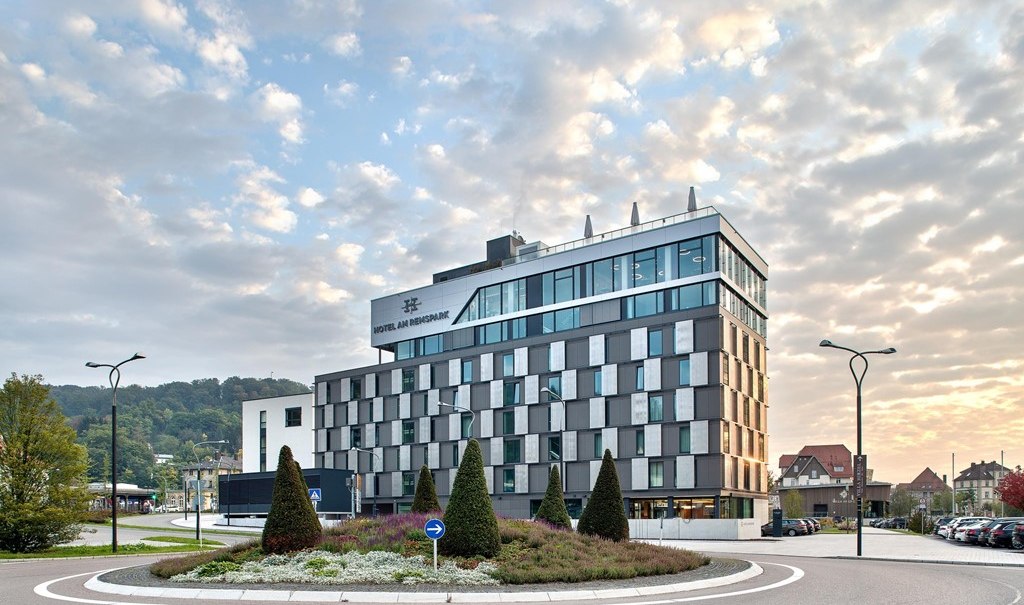 Modern hotel building with glass fa&ccedil;ade, surrounded by a traffic circle and well-kept landscaping, at sunset., &copy; Hotel am Remspark