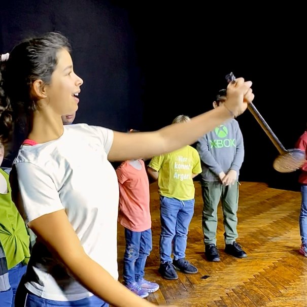 Kinder stehen auf einer Bühne bei einer Generalprobe. Ein Mädchen hält ein Mikrofon und scheint zu singen oder zu sprechen., © Tathea - Lena Oschowitzer Kinder stehen auf einer Bühne bei einer Generalprobe. Ein Mädchen hält ein Mikrofon und scheint zu singen oder zu sprechen., © Tathea - Lena Oschowitzer