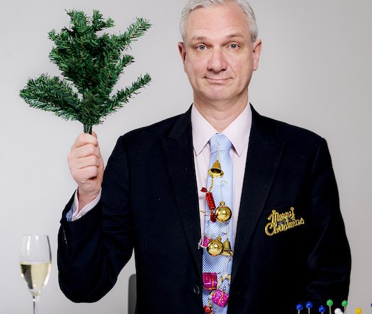 Mann in Anzug mit Weihnachtsdeko hält Tannenzweig. Vor ihm Sektglas und Snacktablett. Hintergrund neutral., © Rosenau Kultur e.V.