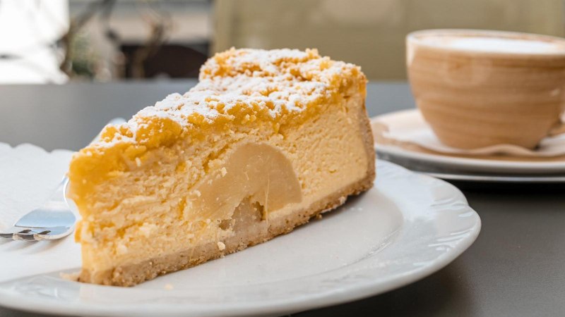 Ein St&uuml;ck Kuchen mit Puderzucker auf einem Teller, daneben eine Tasse Kaffee auf einem Tisch im Caf&eacute; Schurr., &copy; SMG, Sarah Schmid