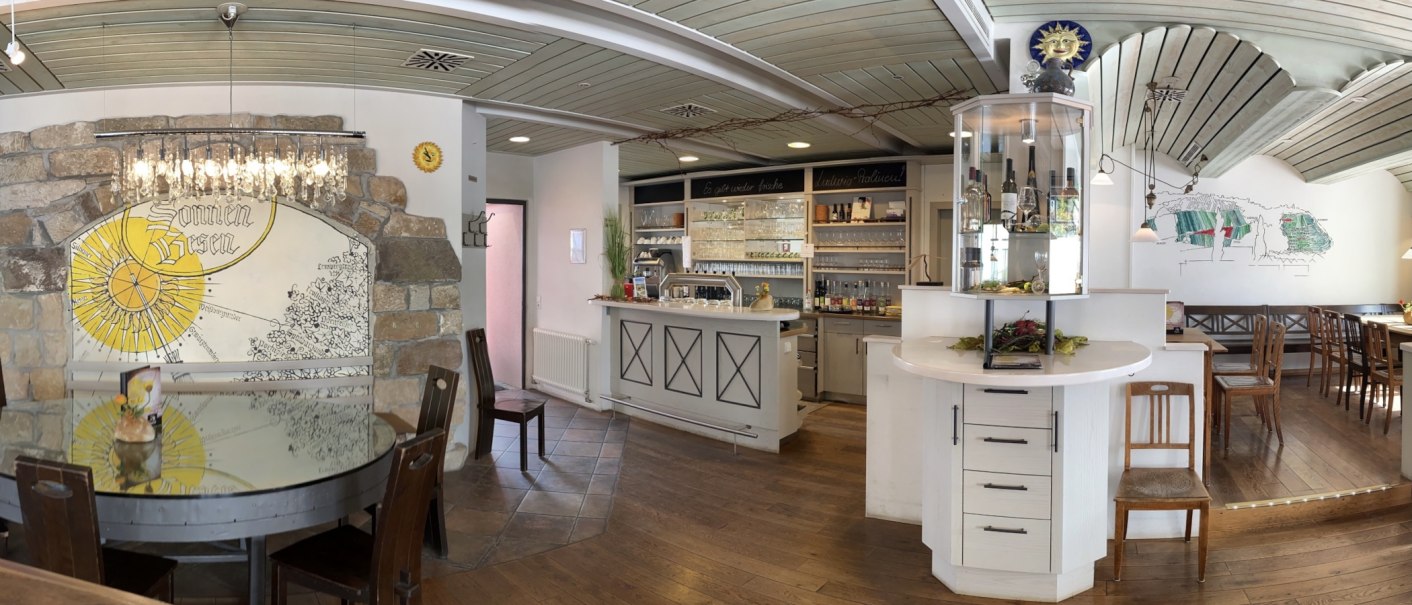 Rustic restaurant with wooden furniture, bar and decorative wall with "sun broom" motif. Cozy atmosphere with chandelier and wine rack., © Weingut Zaiß