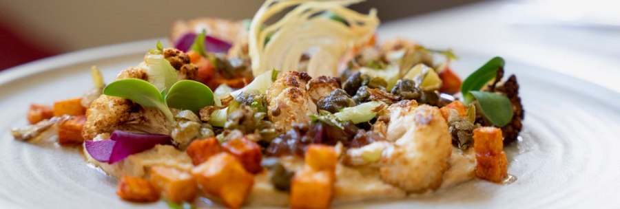 A plate of artfully arranged vegetables, including cauliflower, sweet potatoes and capers, decorated with green leaves and a light sauce., &copy; Veganes Gold&reg;