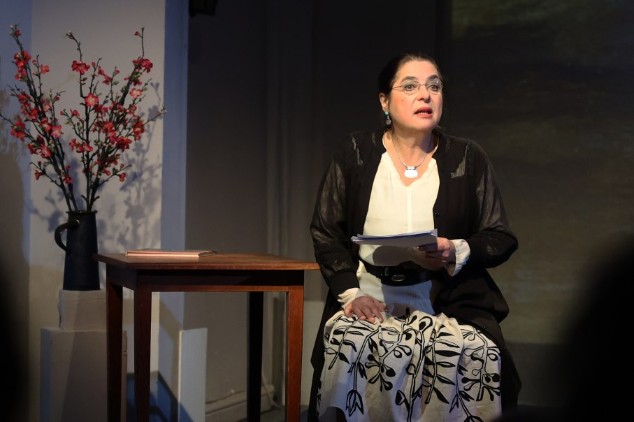 Eine Frau sitzt auf einer B&uuml;hne, h&auml;lt Papiere und tr&auml;gt ein schwarz-wei&szlig;es Outfit. Neben ihr steht ein Tisch mit einer Vase voller Blumen., &copy; Ayman Aljwabra