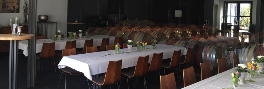 Gedeckte Tische mit Blumen in einer Vinothek, im Hintergrund sind Weinfässer zu sehen. Elegante Atmosphäre mit Holzmöbeln und weißen Tischdecken., © Weingut Wöhrwag Gedeckte Tische mit Blumen in einer Vinothek, im Hintergrund sind Weinfässer zu sehen. Elegante Atmosphäre mit Holzmöbeln und weißen Tischdecken., © Weingut Wöhrwag