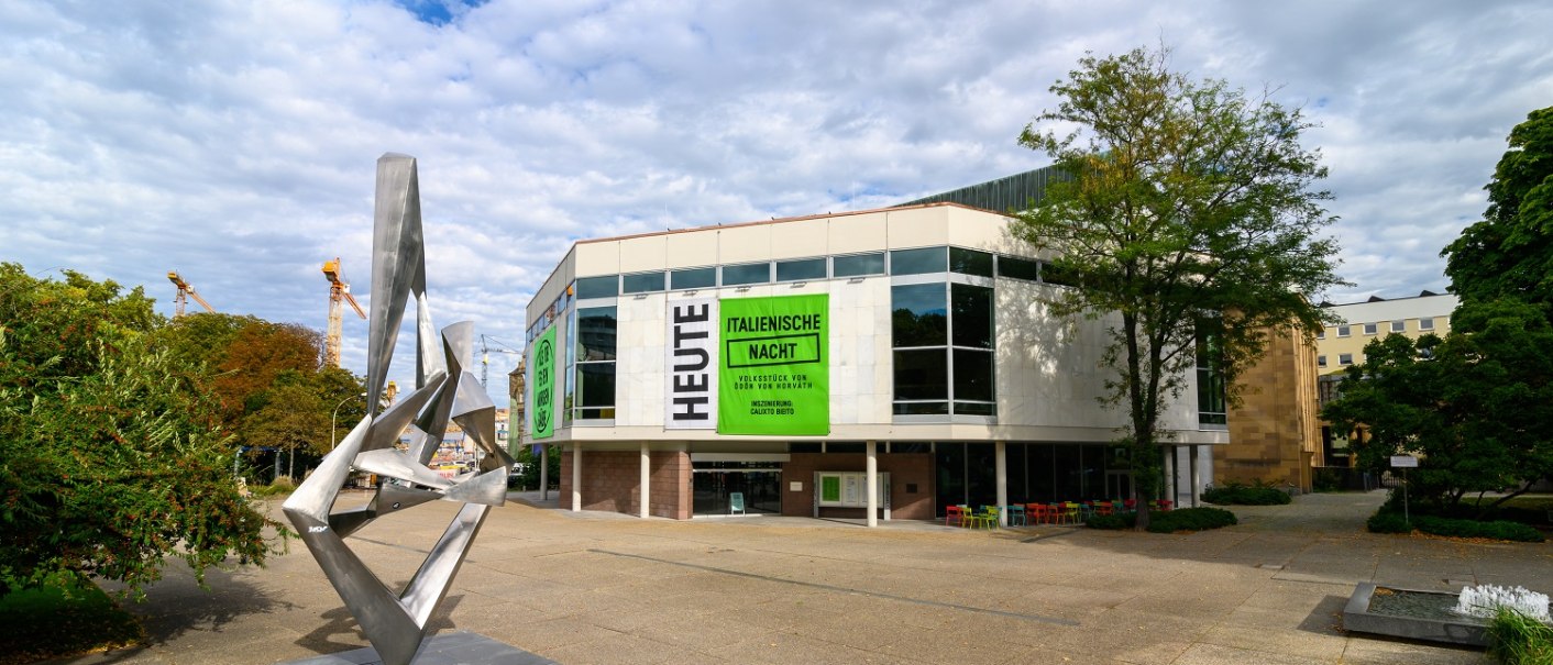 Moderne Skulptur vor dem Schauspielhaus mit gro&szlig;en Fenstern und Plakaten f&uuml;r 'Italienische Nacht'. Wolkenbedeckter Himmel, B&auml;ume und Baukr&auml;ne im Hintergrund., &copy; Bj&ouml;rn Klein