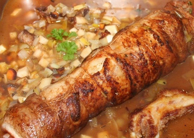 Ein gerollter Braten in einer Pfanne, umgeben von Gem&uuml;sew&uuml;rfeln und einer braunen Sauce, garniert mit einem Petersilienzweig., &copy; Kultweine-Kochwelten-Kunst&uuml;cke - Kochschule Sonja Lenz