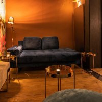 Gemütliche Lounge mit blauer Couch, buntem Wandbild mit Affen und Pflanzen. Im Hintergrund eine Bar mit beleuchteten Regalen und Hockern., © Holzmaler, Stuttgart Gemütliche Lounge mit blauer Couch, buntem Wandbild mit Affen und Pflanzen. Im Hintergrund eine Bar mit beleuchteten Regalen und Hockern., © Holzmaler, Stuttgart