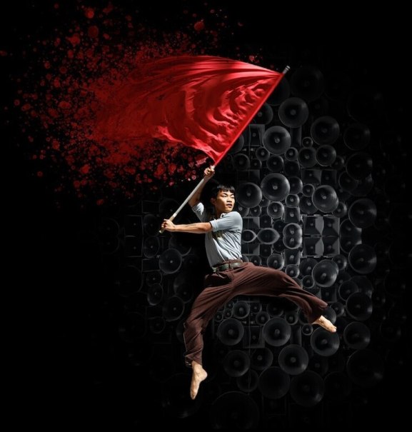 Ein Mann springt dynamisch mit einer roten Fahne vor einer Wand aus Lautsprechern. Der Hintergrund ist dunkel, die Fahne leuchtet kr&auml;ftig rot., &copy; Theaterhaus Stuttgart e.V.