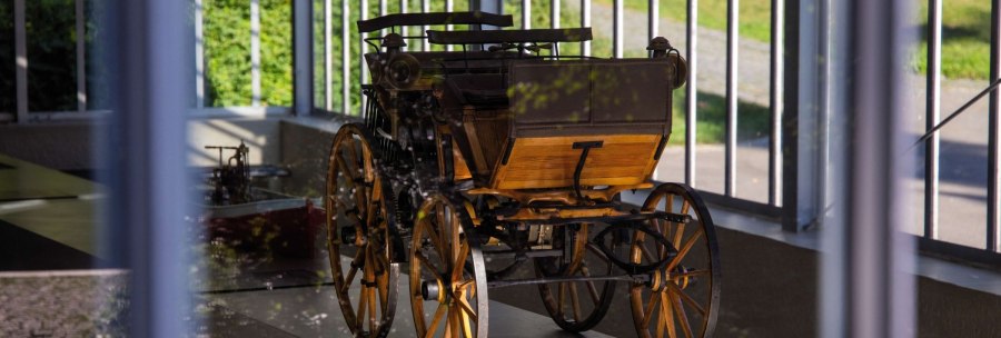 A historic vehicle with wooden wheels stands in a glass pavilion. Sunlight falls through the windows and illuminates the exhibit., &copy; Stuttgart-Marketing GmbH Achim Mende