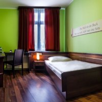 A cozy single room with green-painted walls, a single bed, desk and chair. A red curtain hangs from the window., © TOMAS A cozy single room with green-painted walls, a single bed, desk and chair. A red curtain hangs from the window., © TOMAS