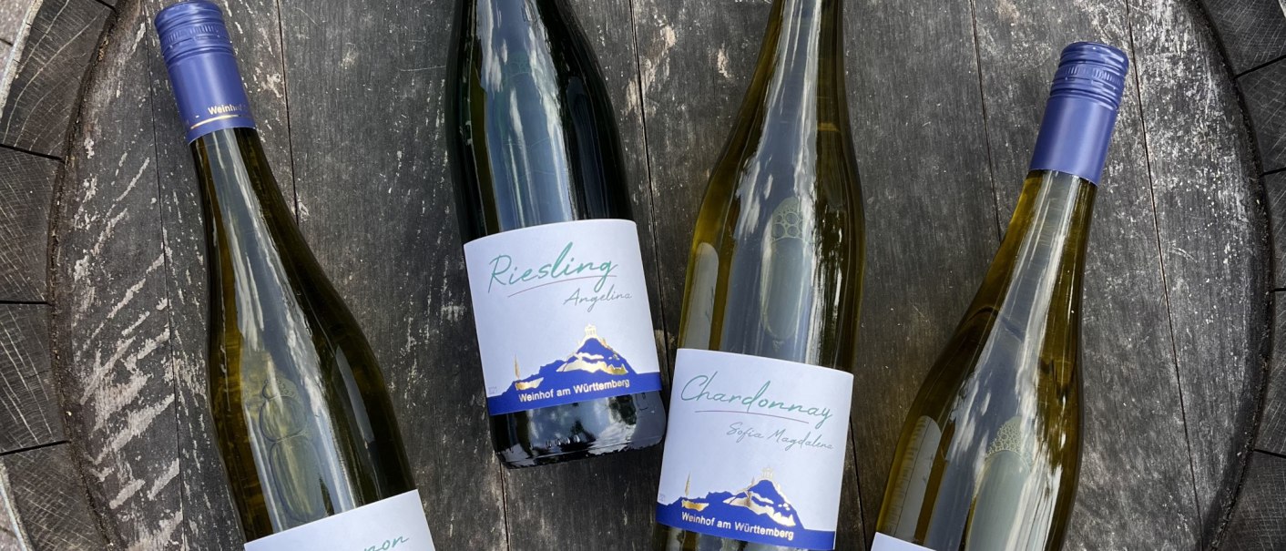 Vier Weinflaschen liegen auf einem Holzfass. Die Etiketten zeigen "Riesling" und "Chardonnay" vom Weinhof am Württemberg., © Weinhof Zaiß Vier Weinflaschen liegen auf einem Holzfass. Die Etiketten zeigen "Riesling" und "Chardonnay" vom Weinhof am Württemberg., © Weinhof Zaiß