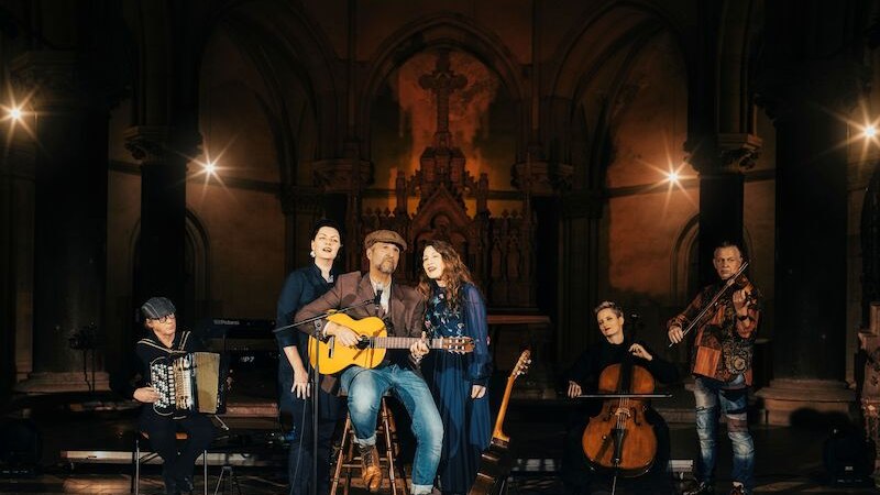 Musikgruppe in einer Kirche, Mann mit Gitarre in der Mitte, umgeben von S&auml;ngern und Instrumentalisten. Stimmungsvolle Beleuchtung., &copy; Live Concept Entertainment GmbH