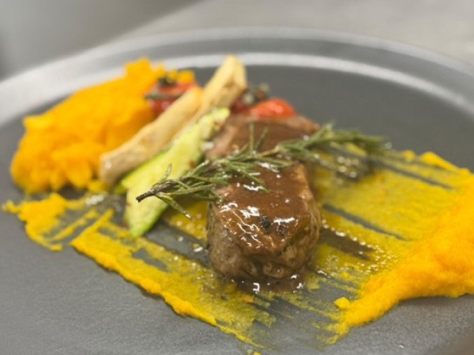 Ein kunstvoll angerichtetes Gericht mit Fleisch, K&uuml;rbisp&uuml;ree und Gem&uuml;se auf einem grauen Teller, dekoriert mit Rosmarin., &copy; Cool-Tours StattReisen