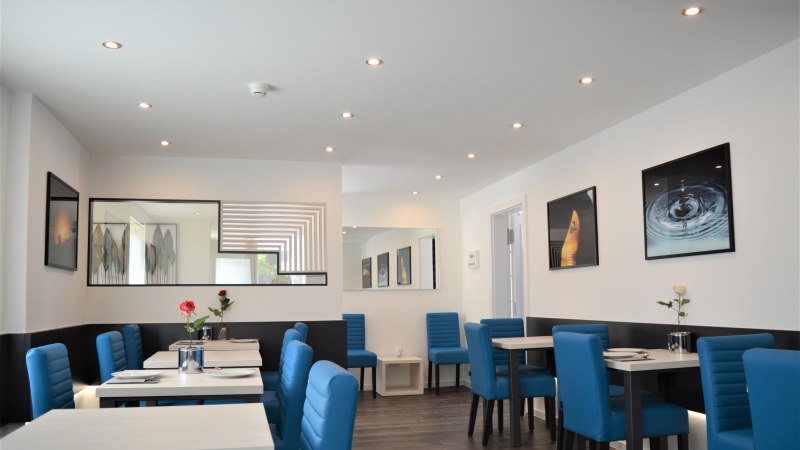 A modern breakfast room with blue chairs, white tables, and decorative pictures on the walls. Subtle lighting and stylish decor., © Hotel BaWü A modern breakfast room with blue chairs, white tables, and decorative pictures on the walls. Subtle lighting and stylish decor., © Hotel BaWü