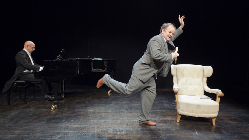Ein Pianist am Flügel und ein Mann in Anzug mit Banane auf der Bühne. Ein Sessel steht daneben., © Foto: Bernhard Fuchs, CH-8135 Langnau am Albis