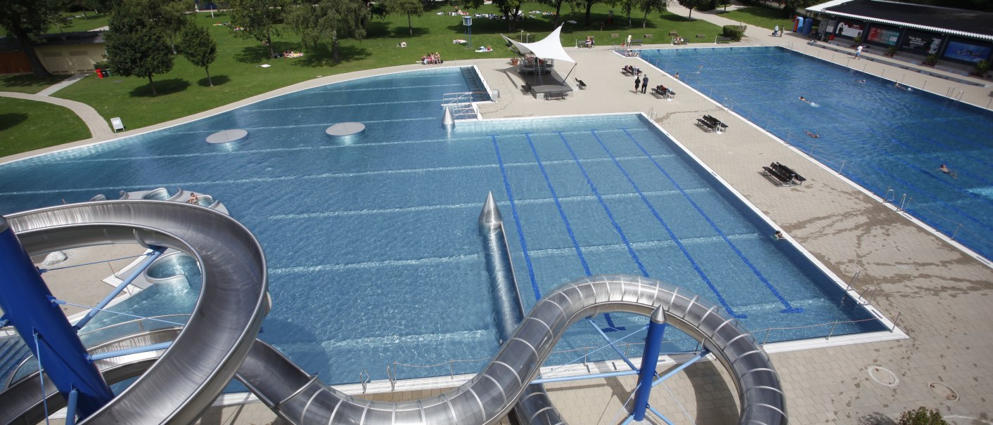 Freibad Rosental mit großer Wasserrutsche, mehreren Schwimmbecken und umliegenden Grünflächen. Menschen entspannen auf der Wiese., © Stuttgarter Bäder Freibad Rosental mit großer Wasserrutsche, mehreren Schwimmbecken und umliegenden Grünflächen. Menschen entspannen auf der Wiese., © Stuttgarter Bäder