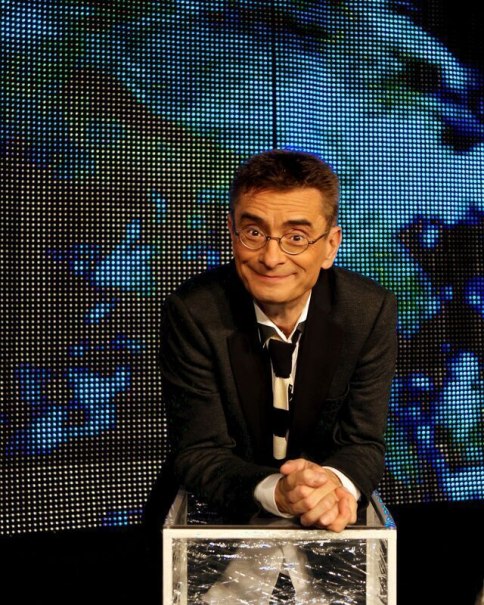 Ein Mann mit Brille und Anzug lehnt sich auf einen gläsernen Tisch vor einem bunten LED-Hintergrund. Er lächelt in die Kamera., © SKS Michael Russ GmbH