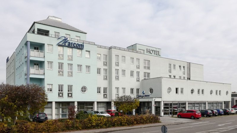 Mehrstöckiges Hotel mit dem Namen Marconi, helle Fassade, geparkte Autos und Bäume im Vordergrund., © Hotel Südtor Mehrstöckiges Hotel mit dem Namen Marconi, helle Fassade, geparkte Autos und Bäume im Vordergrund., © Hotel Südtor