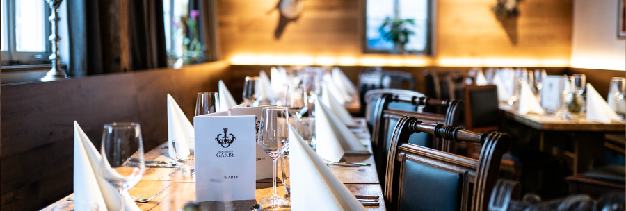 Elegantes Restaurant mit gedecktem Tisch, weißen Servietten und Weingläsern, Holzwände und Geweihdekoration., © Cara Schmid