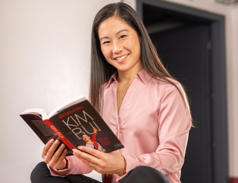 Eine Person in rosa Bluse liest lächelnd ein Buch mit dem Titel '45 Sekunden. Kim Bui'., © Kim Bui