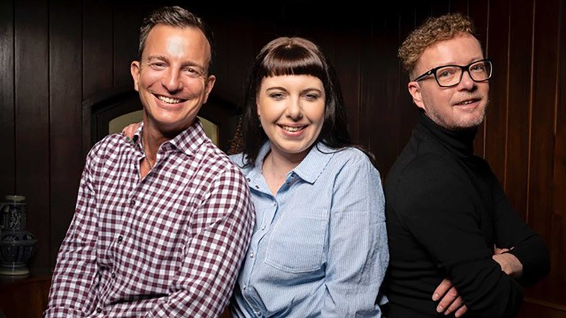 Three people stand smiling next to each other in front of a wooden wall. They are wearing casual clothes and appear cheerful., © Zumbecher Three people stand smiling next to each other in front of a wooden wall. They are wearing casual clothes and appear cheerful., © Zumbecher