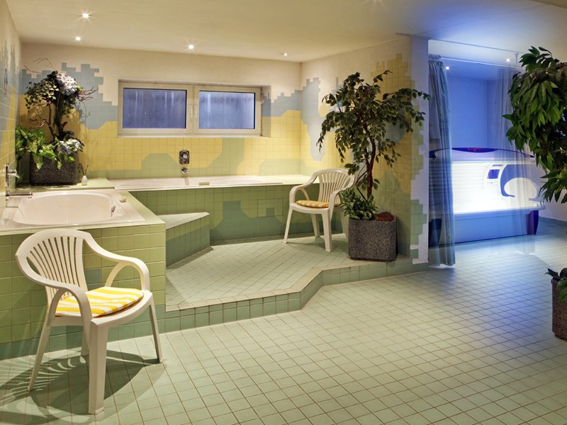 Ein Wellnessbereich mit Whirlpool, Solarium, grünen Fliesen und Pflanzen. Zwei weiße Plastikstühle mit gelben Kissen stehen bereit., © © H-Hotels.com Ein Wellnessbereich mit Whirlpool, Solarium, grünen Fliesen und Pflanzen. Zwei weiße Plastikstühle mit gelben Kissen stehen bereit., © © H-Hotels.com