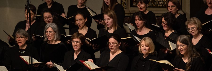 Women's choir in black clothing singing in a church, holding sheet music. Background with decorative writing., &copy; www.hassfoto.de