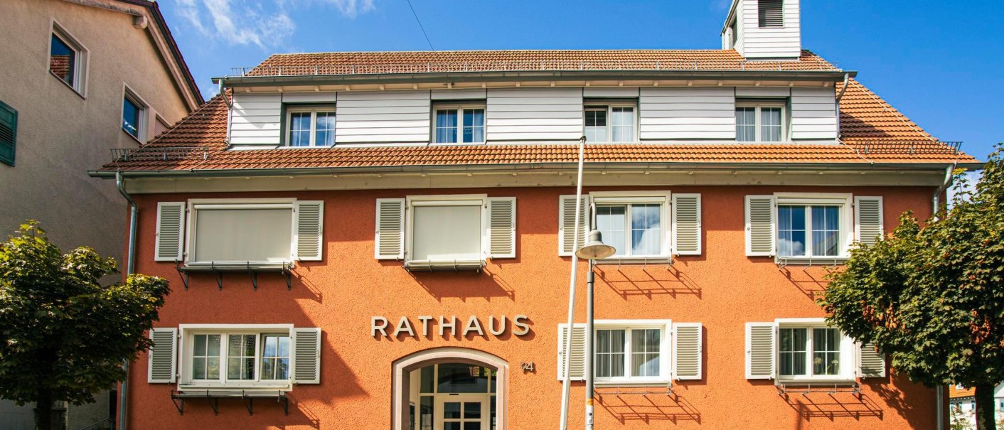Bad Boll town hall with orange façade, white shutters and small tower. There are benches and bicycles in front of the building, surrounded by trees., © Stuttgart-Marketing GmbH, Sarah Schmid