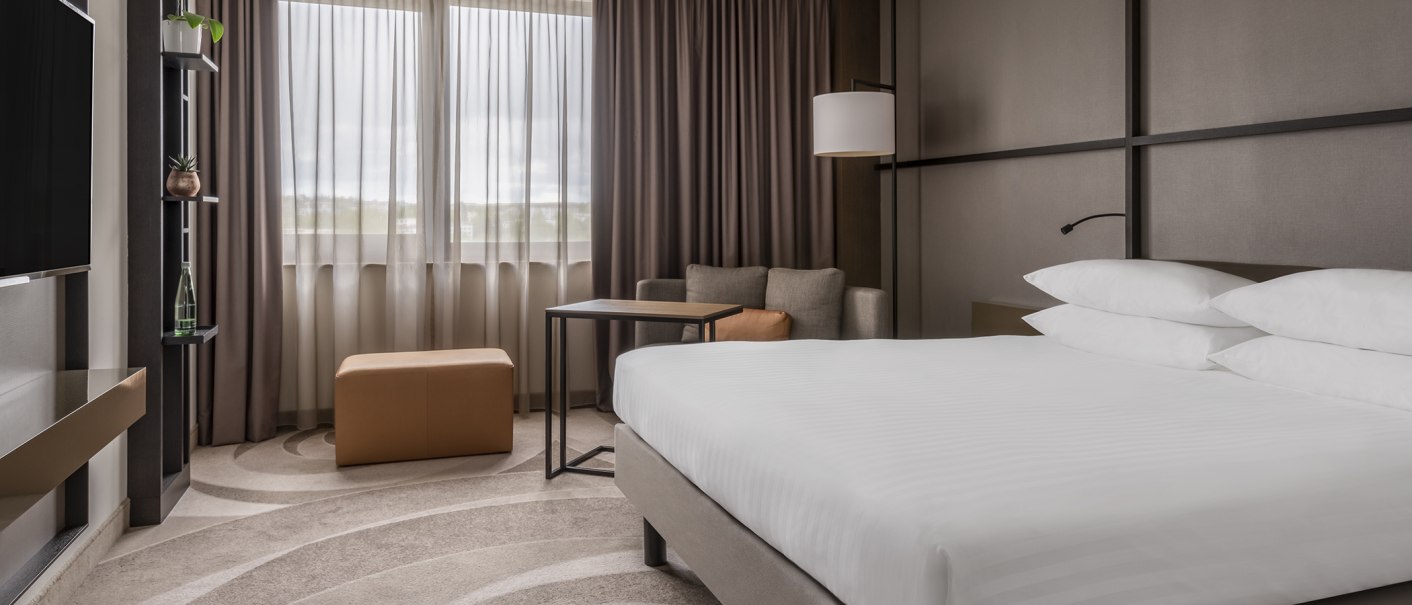 Modern double room with large bed, sofa, table and window with curtains. Subtle colors and stylish furnishings., © Stuttgart Marriott Hotel Sindelfingen Modern double room with large bed, sofa, table and window with curtains. Subtle colors and stylish furnishings., © Stuttgart Marriott Hotel Sindelfingen