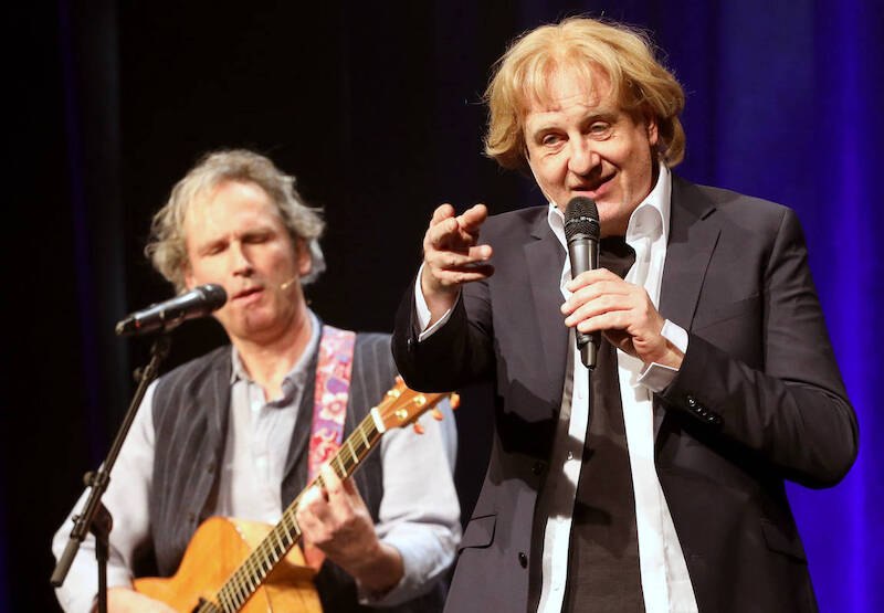 Zwei Männer auf der Bühne, einer singt ins Mikrofon, der andere spielt Gitarre. Hintergrund in Blau., © Theaterhaus Stuttgart e.V. Zwei Männer auf der Bühne, einer singt ins Mikrofon, der andere spielt Gitarre. Hintergrund in Blau., © Theaterhaus Stuttgart e.V.