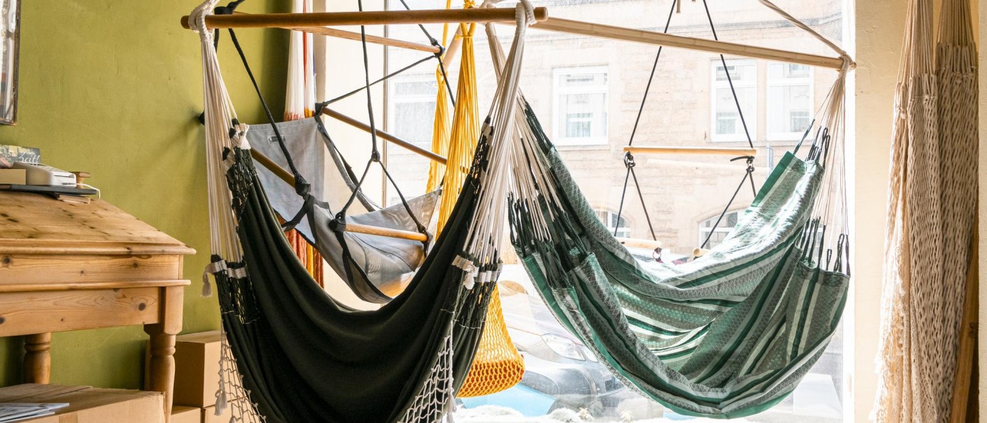 Interior view of a store with several hammocks in different colors hanging in front of a large window. A wooden table stands next to it., &copy; SMG, Sarah Schmid