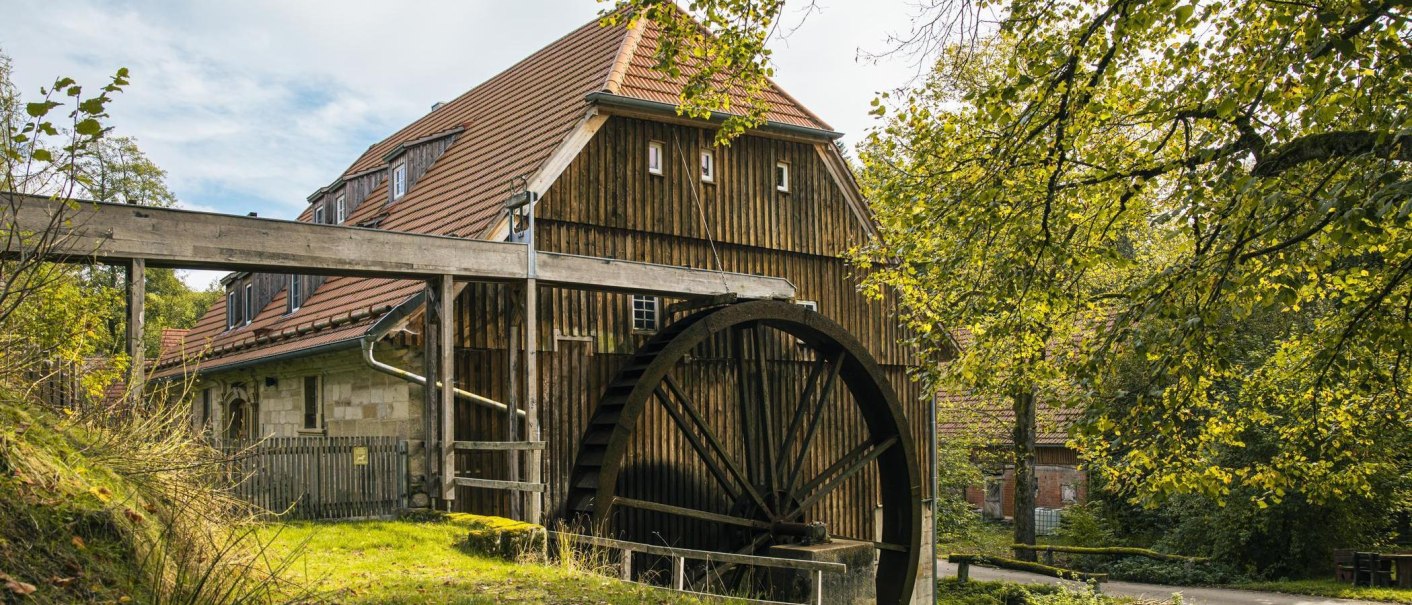 A historic watermill with a large waterwheel and a half-timbered building, surrounded by lush greenery and trees., &copy; SMG Stuttgart Marketing GmbH - Sarah Schmid
