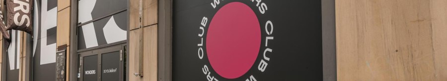 Eingang des Wonders Club mit großem Logo und Schriftzug an der Fassade. Schwarze Türen und ein pinker Kreis mit dem Text 'Wonders Club'., © Stuttgart Marketing GmbH, Sarah Schmid