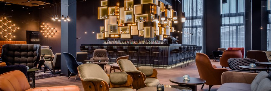 Elegante Bar mit modernen Möbeln, beleuchteten Regalen und gemütlicher Atmosphäre. Dunkle Farben und stilvolle Beleuchtung dominieren den Raum., © TOMAS Elegante Bar mit modernen Möbeln, beleuchteten Regalen und gemütlicher Atmosphäre. Dunkle Farben und stilvolle Beleuchtung dominieren den Raum., © TOMAS