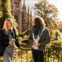 Two people are talking in front of St. John's Church on the Feuersee, surrounded by autumn leaves and sunshine., &copy; SMG, Sarah Schmid