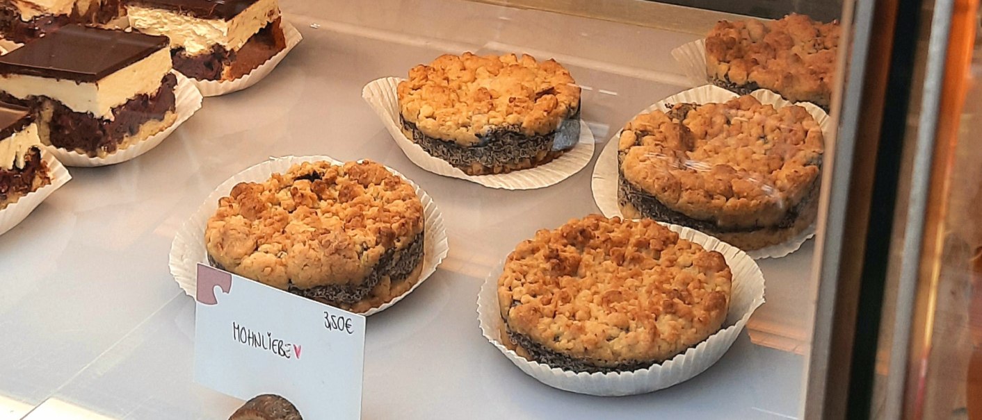 Poppy seed cake and chocolate cake are displayed in a showcase. A sign shows the price of &euro;3.50 for the poppy seed cake., &copy; SMG