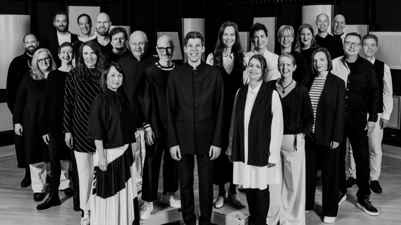 Das SWR Vokalensemble posiert in einem Raum, alle in schwarz-wei&szlig;er Kleidung, l&auml;chelnd in die Kamera schauend., &copy; Lena Semmelroggen