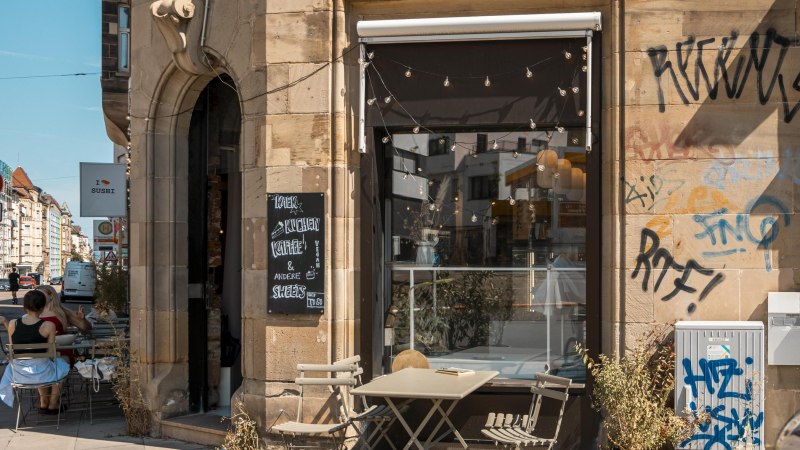 Café with outdoor seating, graffiti on the wall, fairy lights above the entrance. Sign with "Coffee & cake". City street in the background., © SMG Stuttgart Marketing GmbH - Sarah Schmid