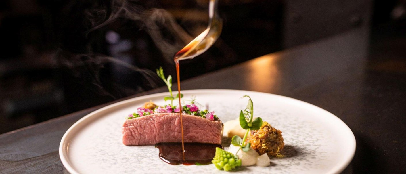 An artfully prepared gourmet dish with meat, vegetables and a dark sauce that is poured onto the plate from a ladle., © 5 - Stuttgart An artfully prepared gourmet dish with meat, vegetables and a dark sauce that is poured onto the plate from a ladle., © 5 - Stuttgart