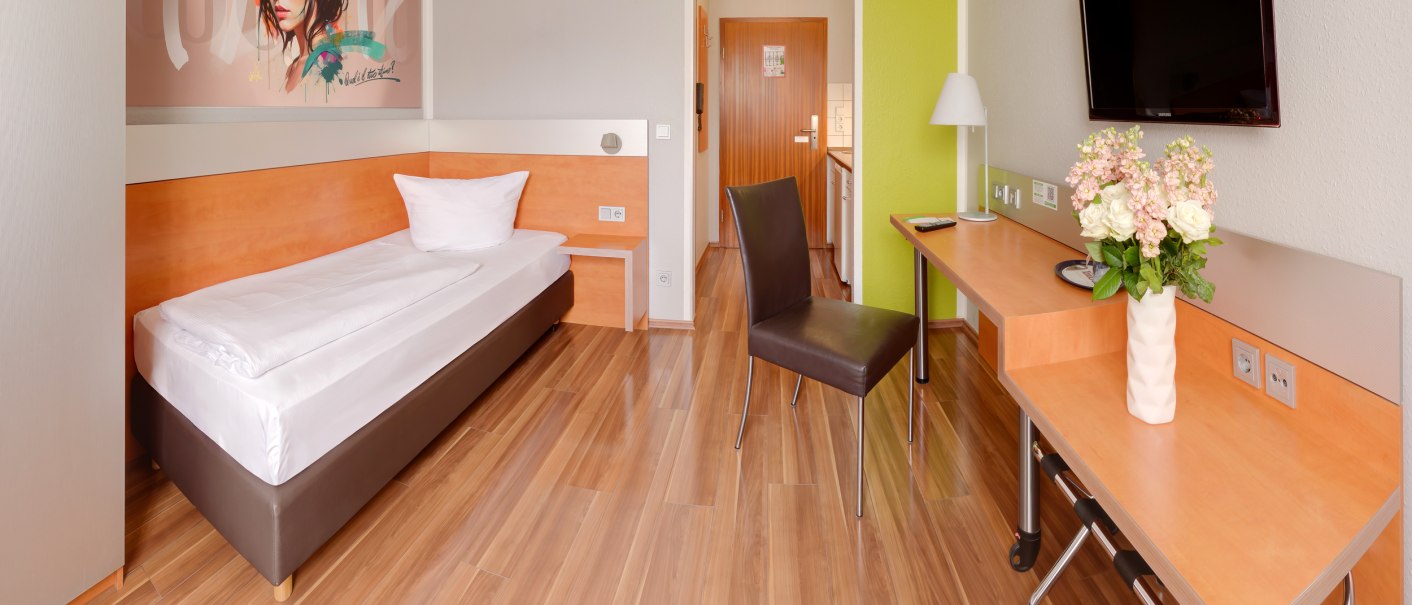 Modernes Einzelzimmer mit Bett, Schreibtisch, Stuhl und Wandkunst. Helle Holzböden, Flachbildfernseher und Blumen auf dem Tisch., © attimo Hotel Stuttgart Modernes Einzelzimmer mit Bett, Schreibtisch, Stuhl und Wandkunst. Helle Holzböden, Flachbildfernseher und Blumen auf dem Tisch., © attimo Hotel Stuttgart