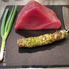 Thunfisch, Wasabi-Wurzel und Frühlingszwiebeln auf einem Schneidebrett, bereit für die Zubereitung., © links im Bild Thunfisch, Wasabi-Wurzel und Frühlingszwiebeln auf einem Schneidebrett, bereit für die Zubereitung., © links im Bild