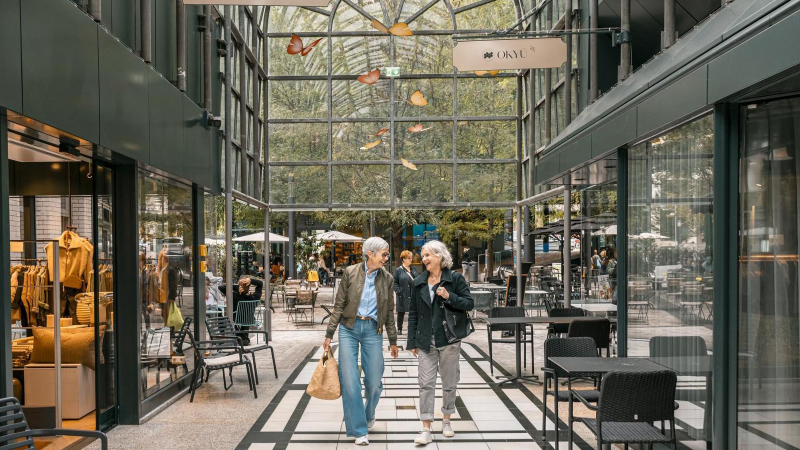 Zwei Personen spazieren durch die Calwer Passage mit Geschäften und Cafés. Die Passage hat ein Glasdach und ist modern gestaltet., © Stuttgart-Marketing GmbH, Sarah Schmid