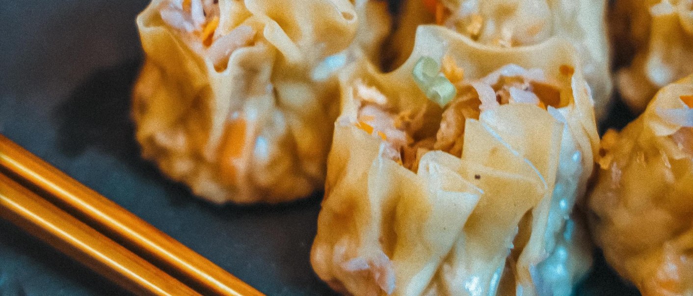 Nahaufnahme von ged&auml;mpften Dumplings mit St&auml;bchen auf einem Teller. Die Dumplings sind gef&uuml;llt und haben eine helle, gl&auml;nzende Oberfl&auml;che., &copy; C&auml;ff Chen, Stuttgart