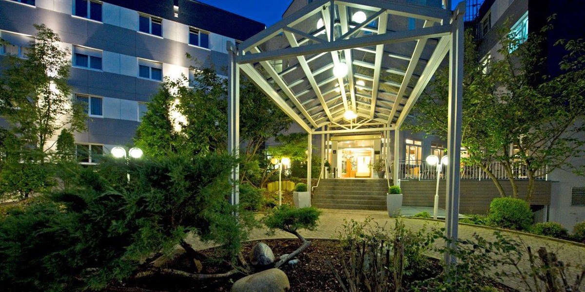 Illuminated hotel entrance at night with glass roof and well-tended garden., © Hotel Fortuna