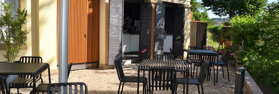 Outdoor area of the 1819 Bistro am Wirtemberg with black tables and chairs on paved ground, surrounded by green vegetation., &copy; 1819 Bistro am Wirtemberg