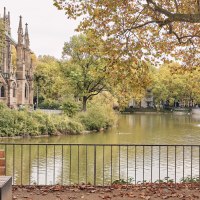 Ein Paar spaziert am Feuersee entlang, im Hintergrund die Johanneskirche und herbstliche Bäume. Ein Brunnen sprudelt im See., © SMG Christoph Düpper Ein Paar spaziert am Feuersee entlang, im Hintergrund die Johanneskirche und herbstliche Bäume. Ein Brunnen sprudelt im See., © SMG Christoph Düpper