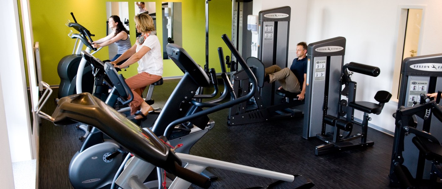 A fitness room with several people working out on different equipment. The walls are painted green., © Hotel Fortuna