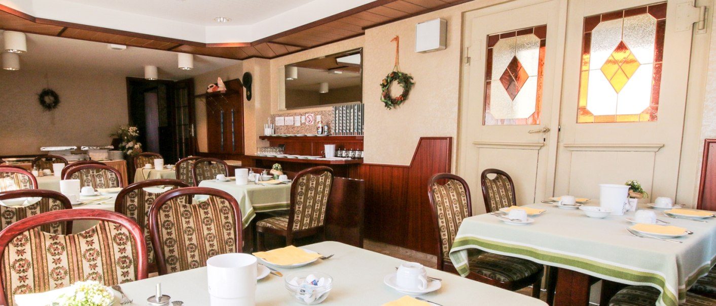 Ein gemütlicher Frühstücksraum mit gedeckten Tischen, Stühlen und dekorativen Elementen. Die Einrichtung wirkt einladend und traditionell., © Ulli Kellenbenz